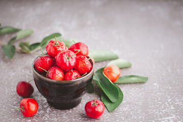 Ripe red cherries in a ceramic bowl with leaves on stone background