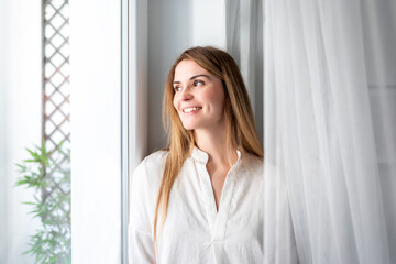 Relaxed young woman looking through window at the morning in home