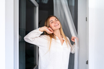 Relaxed young woman looking through window at the morning in home