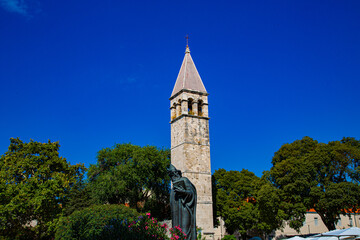 Fototapeta na wymiar Estatua de bronce con torre campanario de arcos y tejado en punta