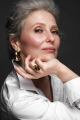 Portrait of a beautiful elderly woman in a white shirt with classic makeup and gray hair.