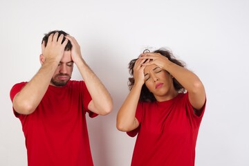 Young beautiful couple wearing red t-shirt on white background suffering from strong headache desperate and stressed because of overwork. Depression and pain concept.