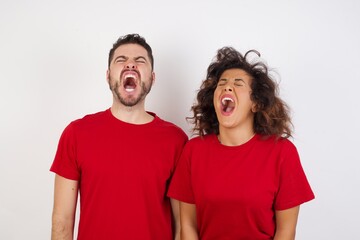 Fototapeta premium Young beautiful couple wearing red t-shirt on white background angry and mad screaming frustrated and furious, shouting with anger. Rage and aggressive concept.