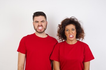 Fototapeta premium Portrait of angry Young beautiful couple , keeps teeth clenched, frowns face in dissatisfaction, irritated because of much duties. Furious man looks out of window, sees miserable weather