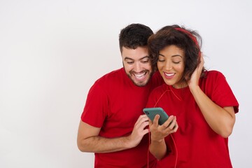 Happy Young beautiful couple wearing red t-shirt on white background  feels good while focused in screen of smartphone. People, technology, lifestyle