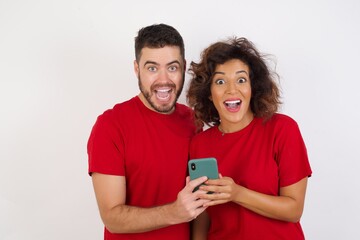 Copyspace photo of cheerful Young beautiful couple wearing red t-shirt on white background holding phone in his hands while