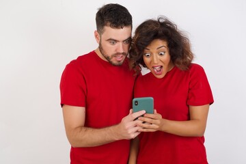 Portrait of nice Young beautiful couple wearing red t-shirt on white background using mobile phone chatting free time .