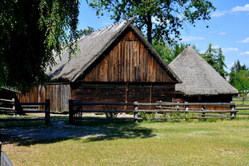 Fototapeta na wymiar View of two farmhouses or barns made out entirely of planks, logs, and boards surrounded with a wooden fence and located next to a vast meadow, pastureland or lawn seen on a sunny summer day in Poland