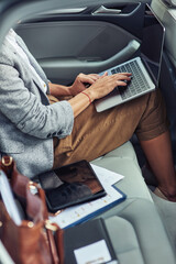 Working online in taxi, vertical shot of business woman using laptop while sitting on back seat in the car
