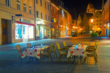 Romantic night scene of street cafe with two tables and old street with citylights on background, Fussen, Germany