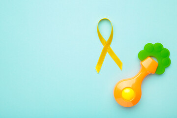 Yellow awareness ribbon and kid toy on blue pastel background with copy space.
