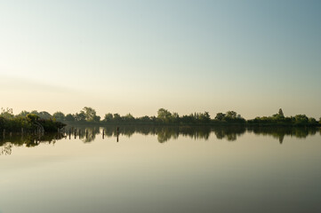 Fototapeta na wymiar Island in the Reeuwijkse plassen in the golden morning light with reflection in the calm water.