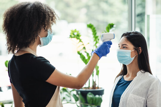 Manager checking body temperature of client at beauty salon, side view
