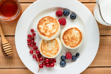Curd cheese fritters, syrniki with fresh summer berries on a plate, wooden background. Top view. Sweet breakfast food