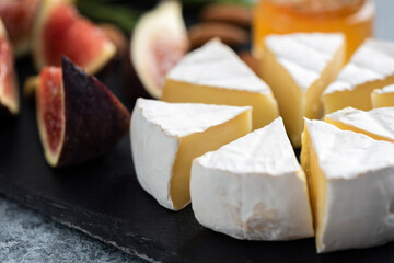 Sliced camembert cheese and figs on black slate, closeup view. Gourmet cheese plate