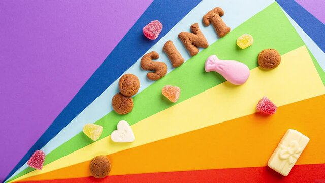Time lapse. Sinterklaas is coming soon, 4K. Dutch holiday St Nicholas day concept with letters, traditional sweets and cookies, kruidnoten on rainbow background with copy space. Top view, overhead.