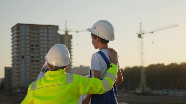 Father and son happy Family concept. Little boy and his dad engineer builder architect with safety helmets, looking on new buildings and construction cranes on site. Future profession, 4 K slow-mo
