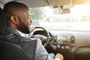 Back view of happy black businessman driving car