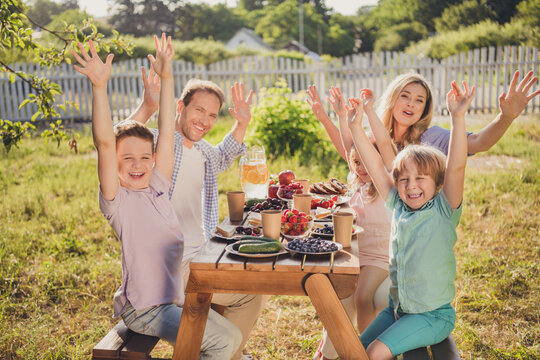 Positive Greeting From Village House. Photo Of Family Gathering Mom Dad Daddy Mommy Small Adopted Kids Sit Table Enjoy Summer Picnic Relax Hold Hands Up Outside