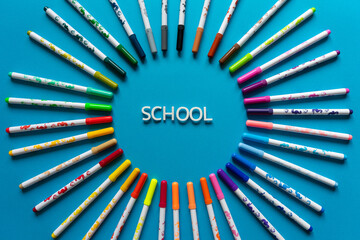 Colored markers laid out in a circle on a blue background. The word school in a circle of markers.