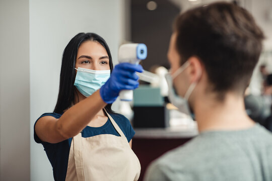 Expert using infrared thermometer to check body temperature of male client at barber shop