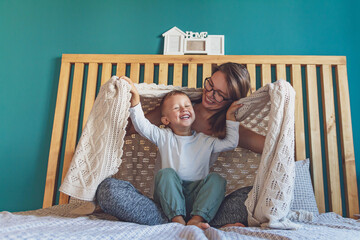 mom and child have fun in the bedroom on the bed under the blank