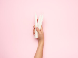 female hand holding a white wax candle on a blue background