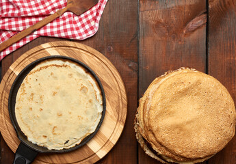 baked round thin pancakes lie stacked on a wooden board, brown table