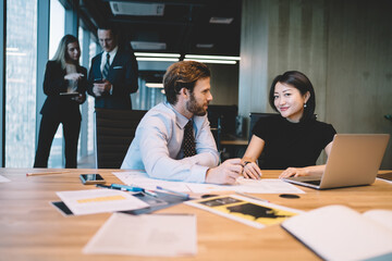 Smiling diverse colleagues at table with laptop and papers