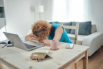 Woman sleeping on her desk at home while working remotely freelance job. Modern problems and issues with working from home.