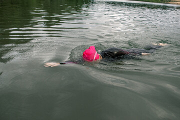 A woman athlete in a pink cap floats on the lake. Sports swimming triathlon.