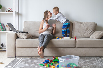 kid plays on the sofa while mom works with tablet, distracts and interferes with mom's work