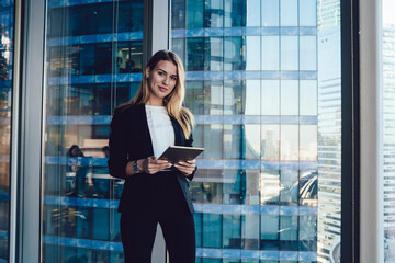 Elegant businesswoman standing with tablet in front of big window