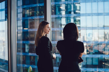 Confident female colleagues dressed in formal wear talking about business in office company,...