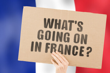 The question " What's going on in France? " on a banner in men's hand with blurred French flag on the background. Protests on the street. Riot. Violence. Economic crisis. Collapse. Politics