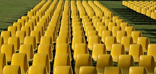 Fototapeta premium Long rows of empty yellow plastic chairs geometrically arranged on a lawn. Texture and background. Copy space..