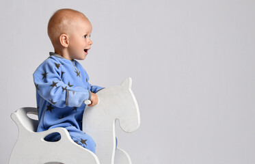 Portrait of happy laughing screaming baby boy in blue fleece jumpsuit with stars riding white kids...