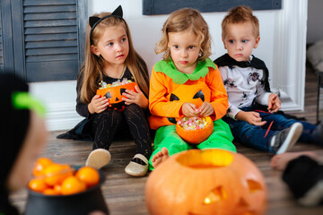 Fototapeta premium Kids in carnival costumes are celebrating Halloween, and playing with pumpkins and candies