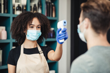 Female beauty master scanning client temperature with touchless thermometer at barbershop