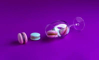 Assorted macarons field with cream in a glass on a purple background.	