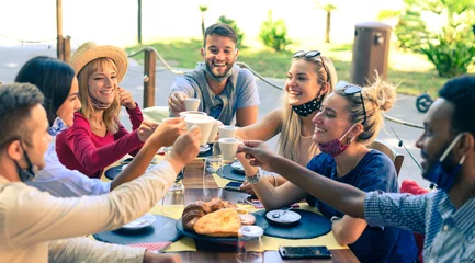 Foto auf Acrylglas Kneipe Gruppe lächelnder Freunde, die eine Schutzmaske tragen und Kaffee und Cappuccino im Bar-Café rösten?