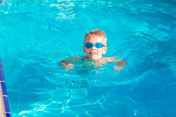 Cute happy little boy in goggles swimming in the swimming pool