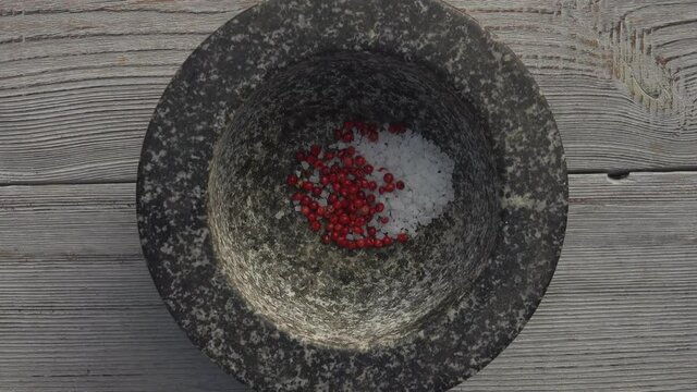 Male hand is putting a variety of peppercorns, sea salt and brown sugar into the mortar and starting to grind
