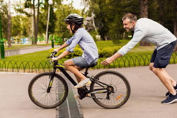 Son learning how to ride bicycle with his happy dad