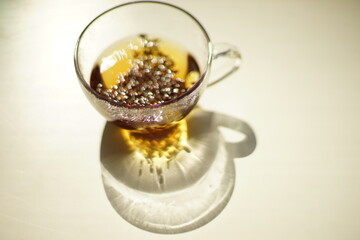 Transparent glass cup with black flower tea on the sunny table.