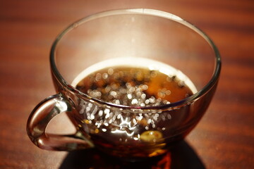 Glass cup with black tea on the brown wooden table. Closeup view