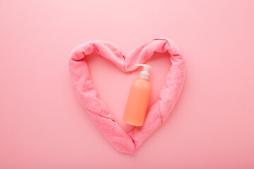 Orange pump bottle of liquid soap and heart shape created from towel on light pink table...