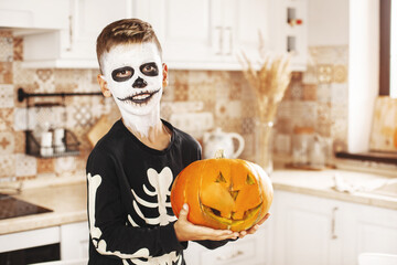 Happy boy dressed as a dead man laughing and holding Jack's pumpkin lantern while celebrating Halloween