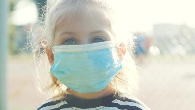 portrait of a little kid girl in a medical protective mask on the playground. concept pandemic covid 19 coronavirus. daughter child kid in a medical mask on the playground. kid in outdoors mask