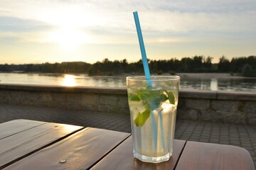 Glass with lemonade or mojito coctail with lemon and mint. Cold refreshing drink with ice and blue straw. 